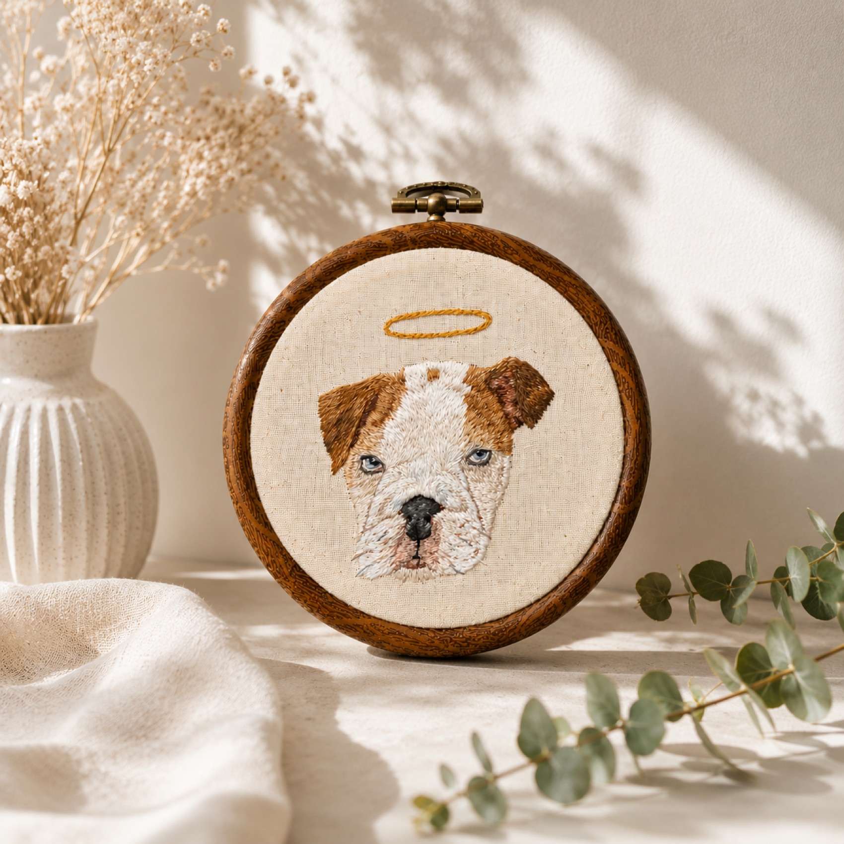 A bulldog with a gold halo, a memorial portrait hand-embroidered on linen.