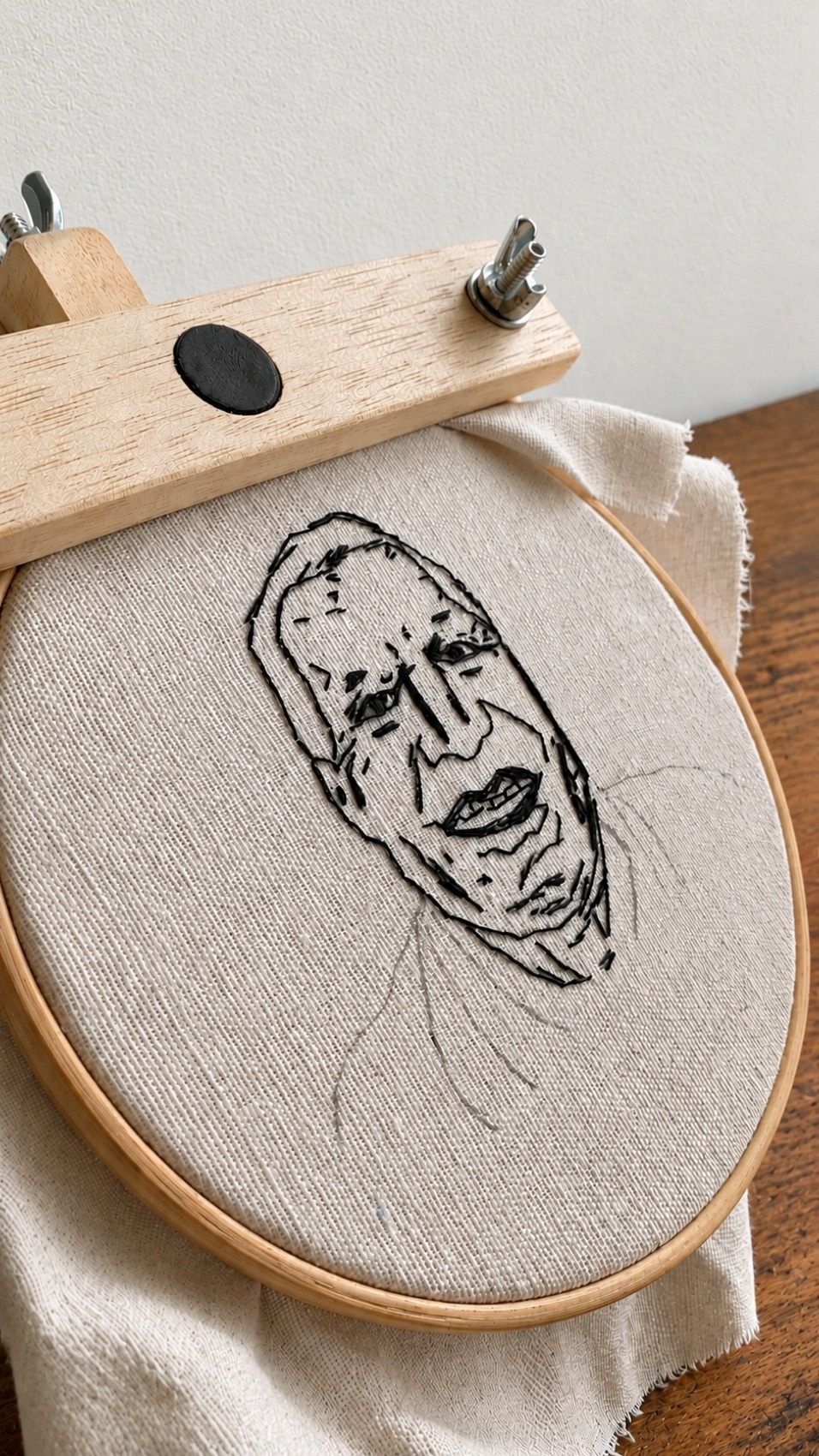 A line portrait of a man's face, hand-embroidered in a single thread on linen.