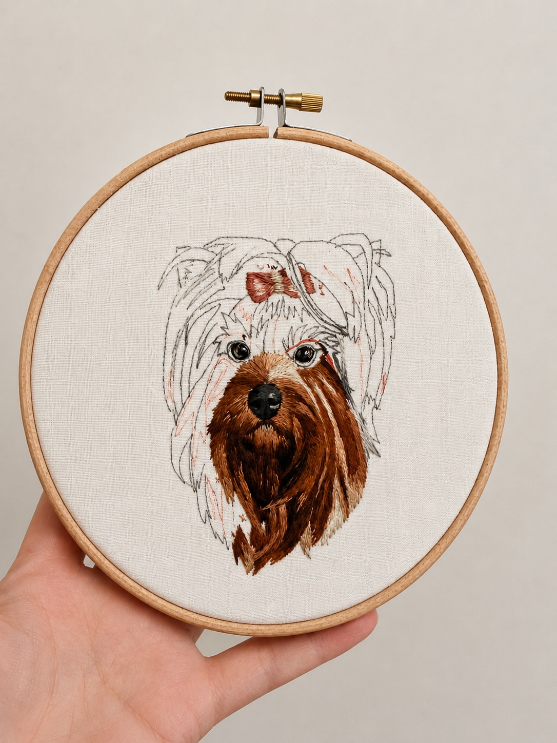 A hand-embroidered Yorkshire terrier portrait, the face stitched in warm browns with the long coat sketched in fine pencil lines, held in a wooden hoop on natural linen.